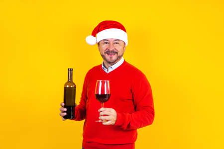 latin senior man in christmas concept holding a glass of wine with santa hat, having fun, smiling...