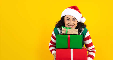 Portrait of Latin mature woman holding Christmas gift box on a yellow background in Mexico latin americaの写真素材