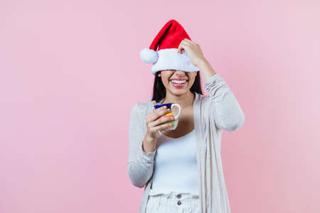 hispanic christmas woman, with a clay mug of coffee or fruit punch on pink background in latin americaの写真素材