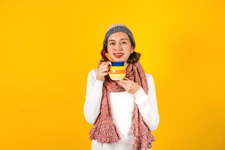 hispanic young woman, with a clay mug of coffee or fruit punch for winter on yellow background in...
