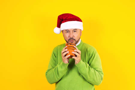 hispanic senior man with a clay mug of coffee or fruit punch in christmas on yellow background in latin americaの写真素材