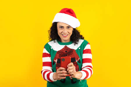 Portrait of adult latin woman using mobile phone with copy space in a christmas concept on yellow...