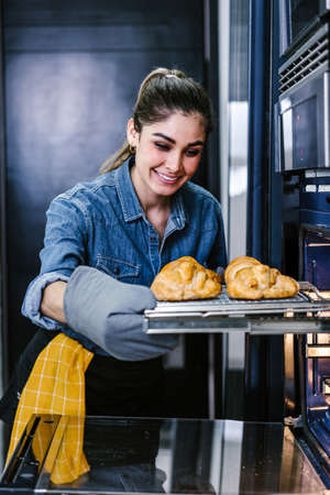 young Latin woman baking croissant on oven in kitchen in Mexico Latin Americaの写真素材