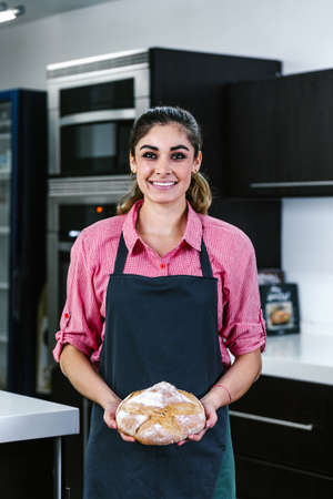 young Latin woman holding piece of bread in kitchen in Mexico Latin Americaの写真素材