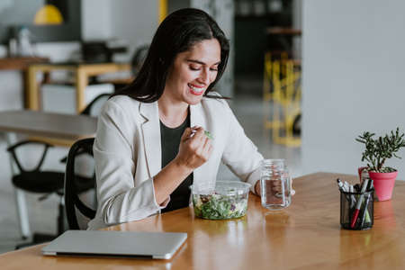 latin adult woman eating salad lunch at the office in Mexico Latin Americaの写真素材