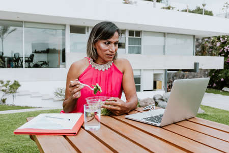 transgender latin woman working with computer and eating salad bowl at the office terrace in Mexico Latin Americaの写真素材