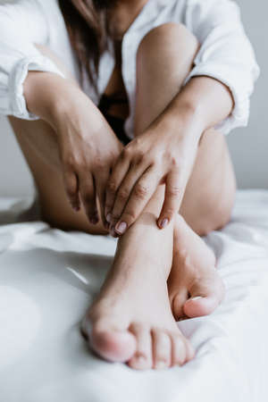 Young Latin woman sitting on bed, wearing white robe, showing legs at home in Mexico city