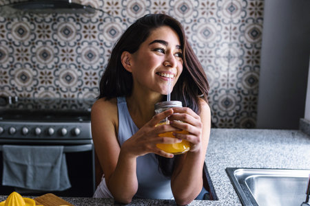 latin woman drinking orange juice while resting on sofa at home in Mexico Latin Americaの写真素材