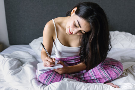latin young girl with computer and notebook on bed at home in Mexico Latin Americaの写真素材