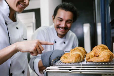 young Latin couple woman and man bakers and baking croissants and bread on oven at kitchen in Mexico Latin Americaの写真素材