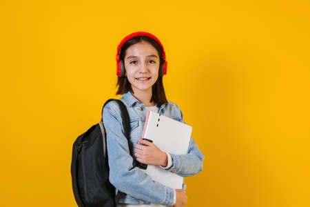 portrait of young hispanic child teen girl student with headphones listening music on a yellow background in Mexico Latin Americaの写真素材
