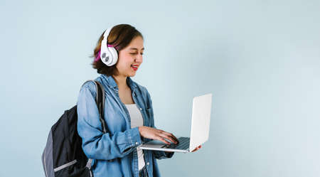 Young Hispanic student woman listen music with headphones and holding computer over isolated blue backgroundの写真素材