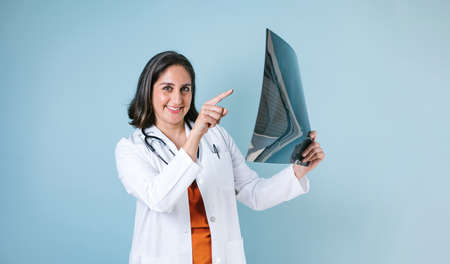 hispanic woman doctor looks at xray radiography images in radiology clinic on blue background in Mexico Latin Americaの写真素材