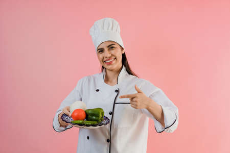 young latin woman wearing chef hat with ingredients to cook mexican food on pink color backgroundの写真素材