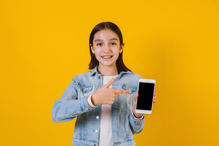 Latin child girl on holding a mobile phone with copy space on yellow background in Mexico Latin Americaの写真素材