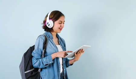 Young Hispanic student woman listen music with headphones and holding digital tablet over isolated blue backgroundの写真素材