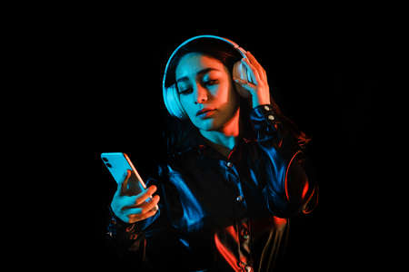 latin young woman with headphones listening to music over color neon and black background in Mexico Latin Americaの写真素材