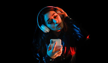 latin young woman with headphones listening to music over color neon and black background in Mexico Latin Americaの写真素材