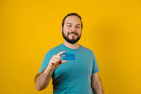 young latin man holding a credit card for shopping on yellow background in Mexico Latin Americaの写真素材