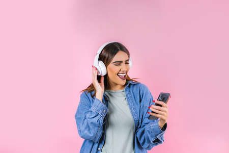hispanic young woman with headphones, dancing and listening music on pink background in Latin Americaの写真素材