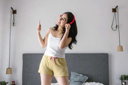 Young latin woman listening music with headphones on bed at home in Mexico Latin Americaの写真素材
