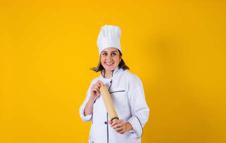cheerful female chef in uniform with rolling pin on yellow backgroundの写真素材