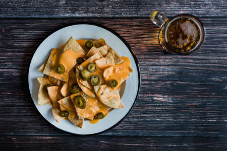 Nachos with cheese sauce and jalapeno peppers on wooden backgroundの写真素材