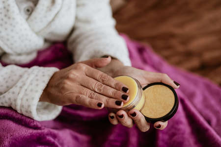 Female hands with brown manicure hold a jar of yellow nail polishの写真素材