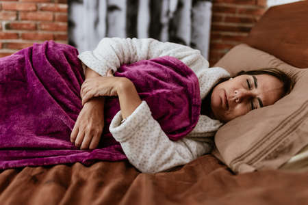 Young woman lying in bed and sleeping. She is wearing a purple bathrobe.の写真素材