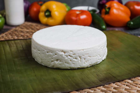 Fresh round white cheese on a green banana leaf and vegetables in the background