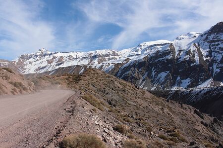 A gravel road between the snowy mountains under a blue sky at day time in the central Andes of Chileの写真素材