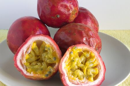 Some passion fruit on a plate. One of the fruit is cut in half, showing the flesh inside