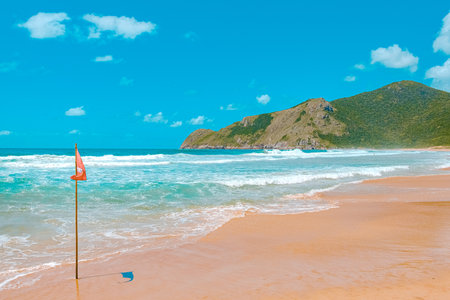 Red flag on the sandy beach with blue sky and mountain background.の写真素材