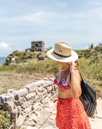 young hispanic woman traveler with hat and backpack looking from above ancient ruins on the coast of the caribbeanの写真素材