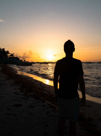 Hispanic man silhouette from the back looks at an incredible sunset on the coast of the Caribbean Seaの写真素材