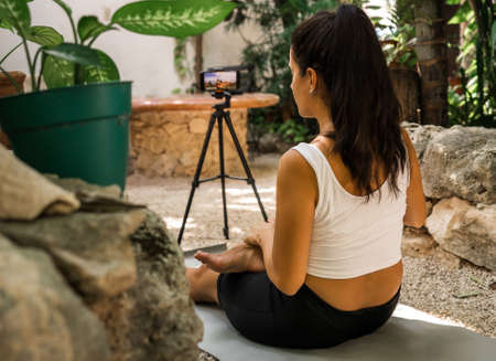 hispanic woman performs an online yoga class in nature from her cell phone