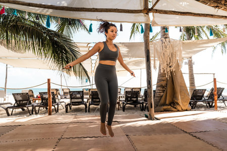 young hispanic woman jumps rope in an eco gym on the beach