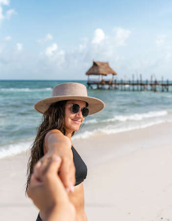 hispanic woman with sunglasses and hat holding her partners hand looking back