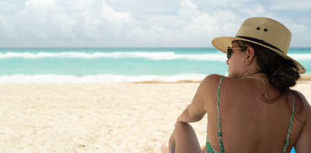 young hispanic woman with sunglasses and hat sitting looking at the seaの写真素材