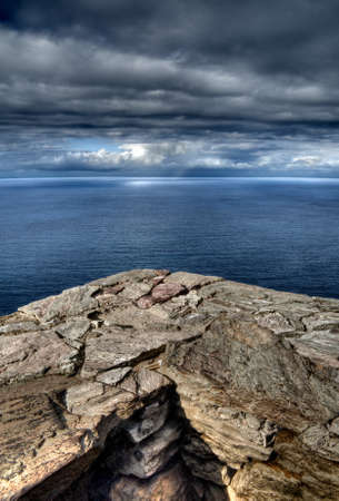A vertical shot of a rocky coastline under a cloudy sky with the ocean in the background