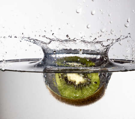 Kiwi falling into water with a splash on a white backgroundの写真素材
