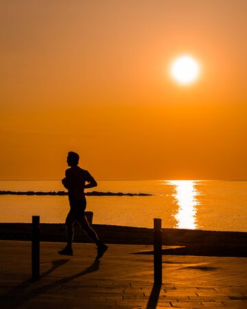 Silouhette of man jogging by the beach at sunriseの写真素材