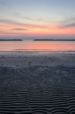 Low tide on the beach at dawn with rocks and sky in the distanceの写真素材