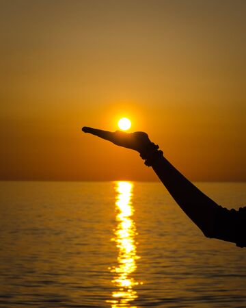 Silhouette of a girl holding the Sun in her hand at sunrise in Barcelonaの写真素材