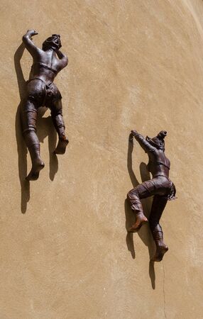 Bronze statues of women climbing the wall of a buildingの写真素材