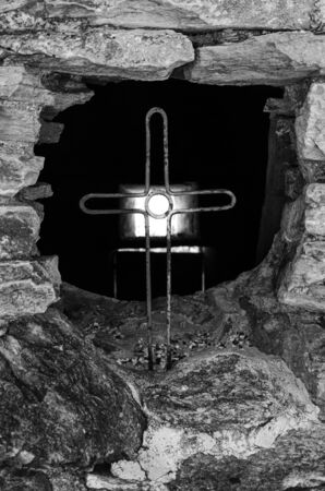 Christian cross made of iron embedded in a rock wall in black and whiteの写真素材