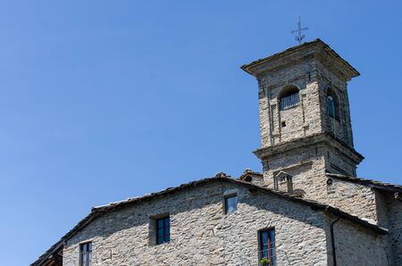 Detail of roof and campanile with cross of old stone chuch in the mountains, against blue skyの写真素材