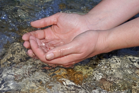 hands of a young woman refreshing in the fresh and pure water of a mountain streamの写真素材