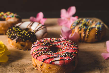 still life colorful donuts on a wooden table with some flowersの写真素材