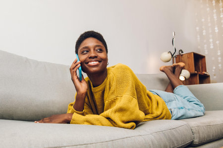 African woman using cellphone at home sitting on the sofaの写真素材